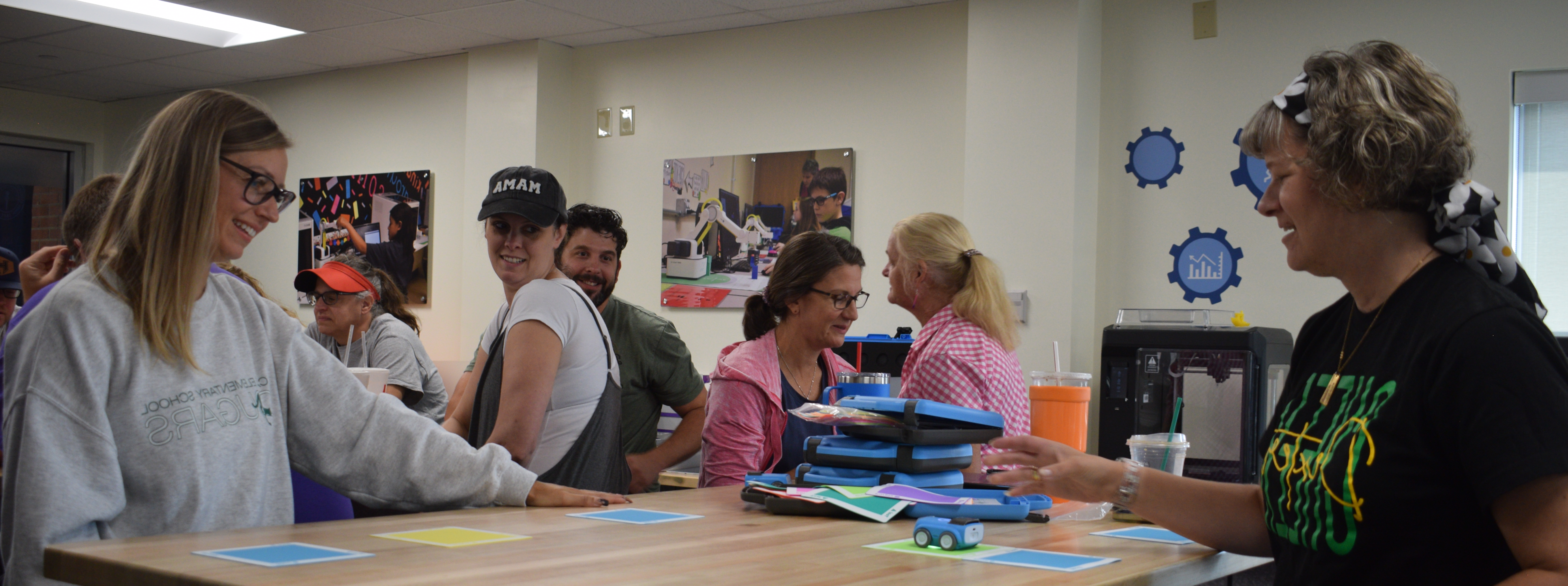 Area female teachers stand at a table demonstrating tiny robot cars, navigating a path of brightly colored squares.